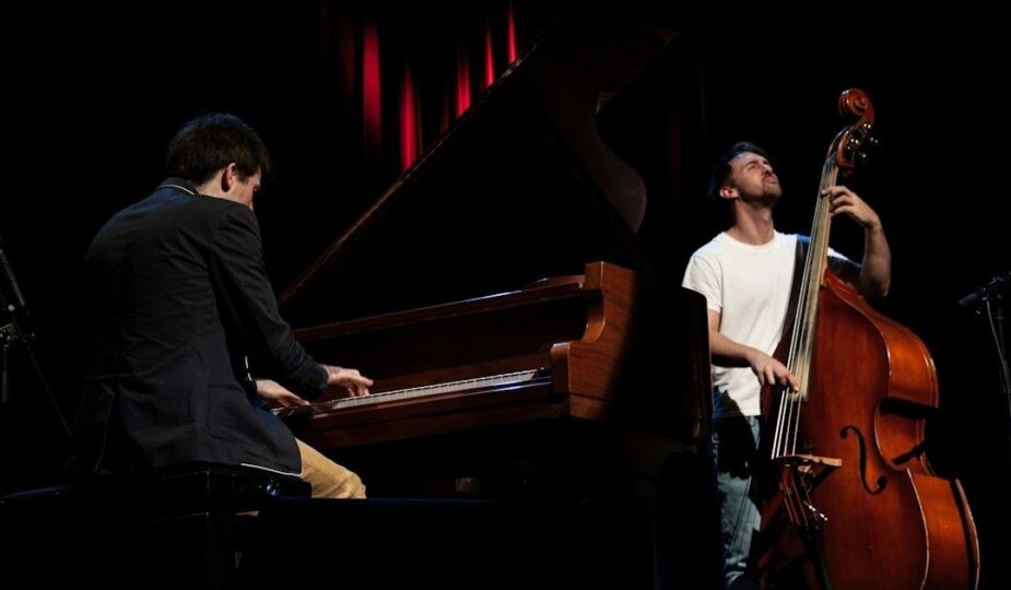 Pianist und Kontrabassist spielen gemeinsam auf einer abgedunkelten Bühne
